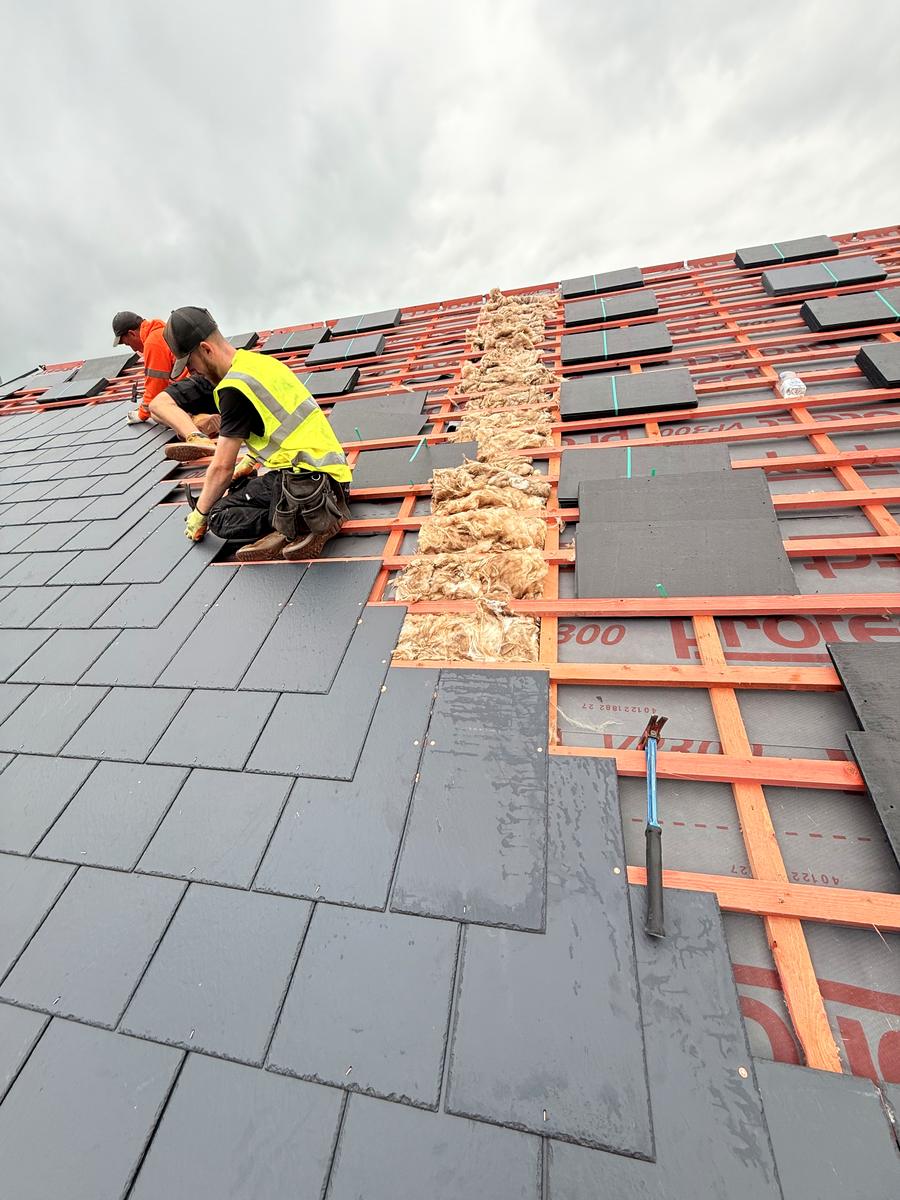 Roofers slating over a breathable membrane on counter-battens, with mineral wool insulation between the rafters